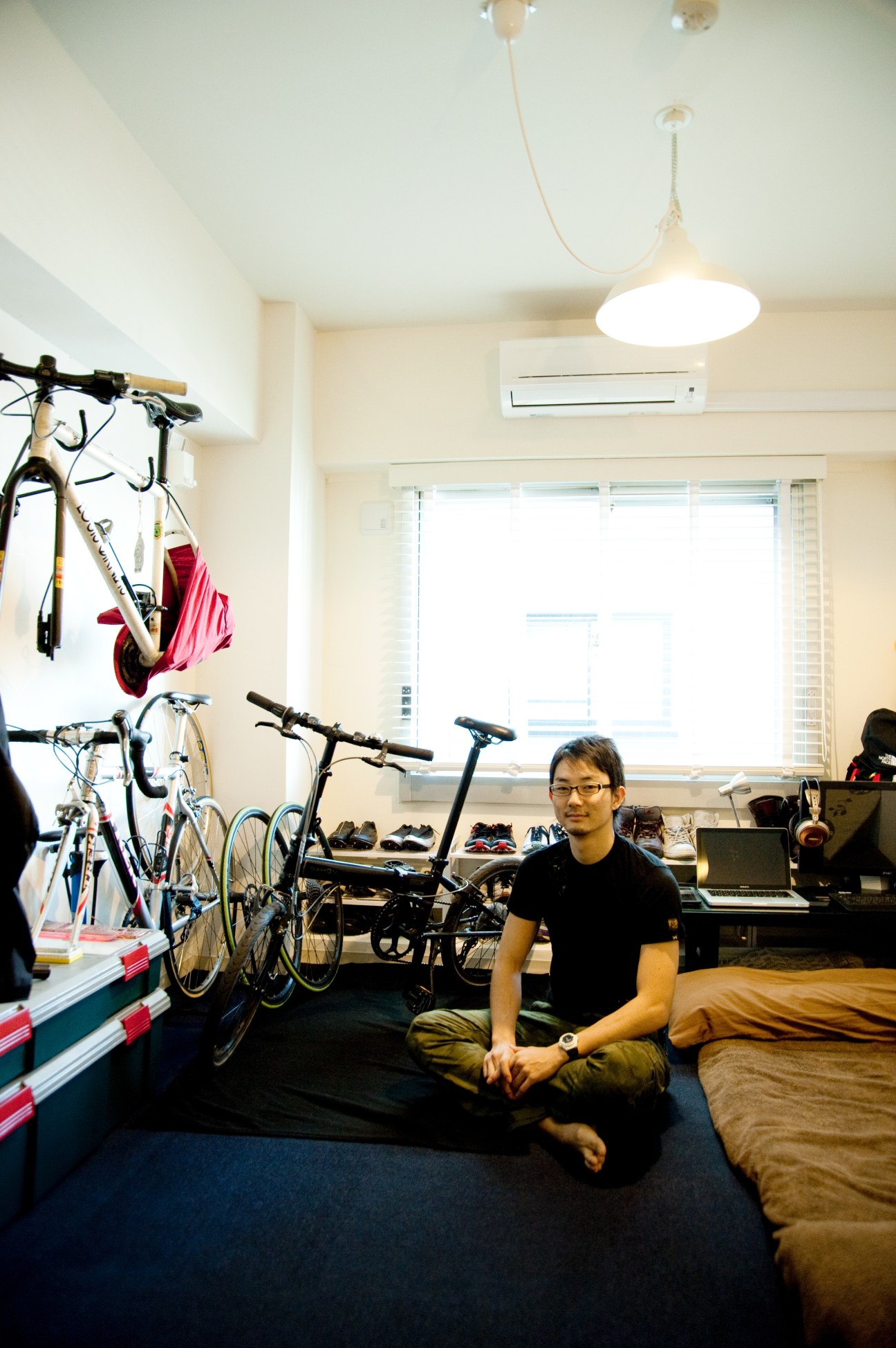 Tsubasa Nishimura sits in his compact studio room at The Share, with bicycles and personal items stored on the walls.