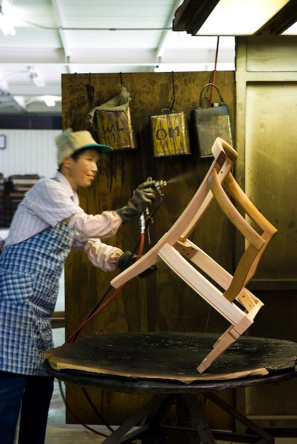 Craftsman hand-finishing a wooden chair frame in a factory workshop.