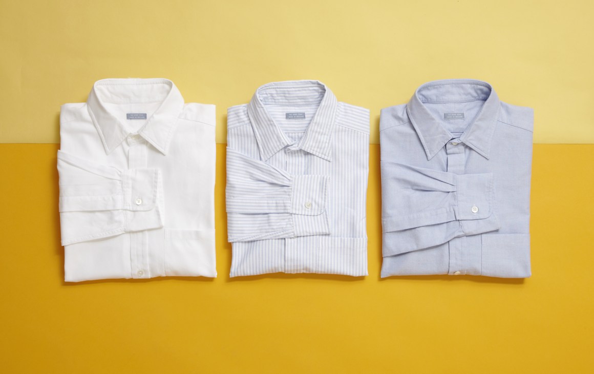 Three folded dress shirts in white, light blue striped, and pale blue against a yellow background.
