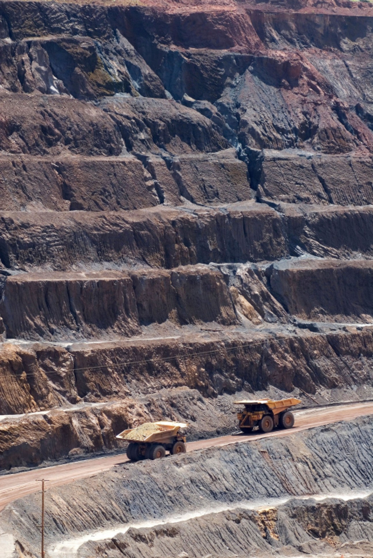 Open pit iron ore mine with terraced rock walls and yellow mining trucks at Congonhas do Campo, Minas Gerais.