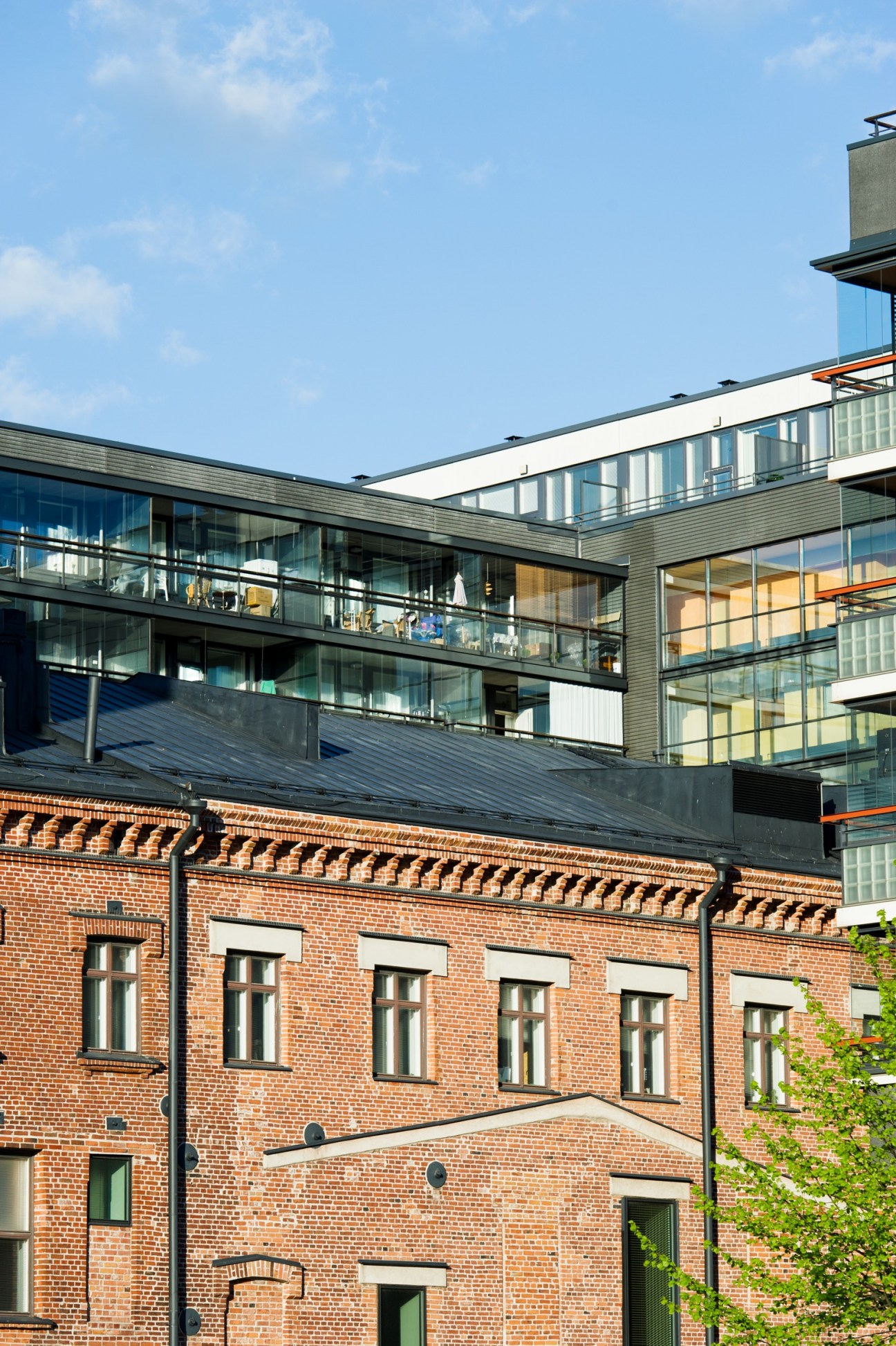 Modern multi-story building with glass balconies and metal railings overlooking a historic red-brick building.