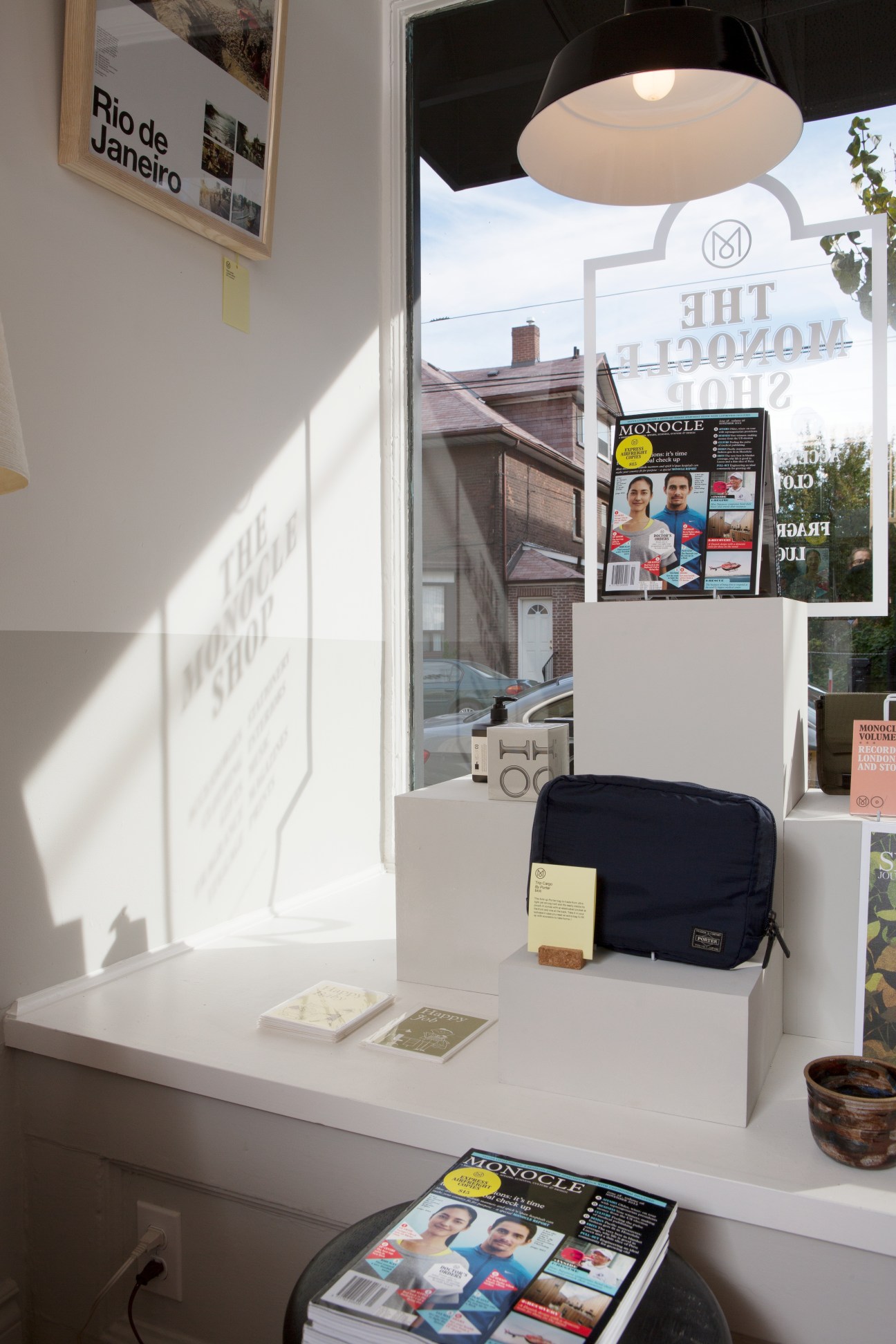 Window display of Monocle Shop Toronto featuring magazines, merchandise and pendant lighting.
