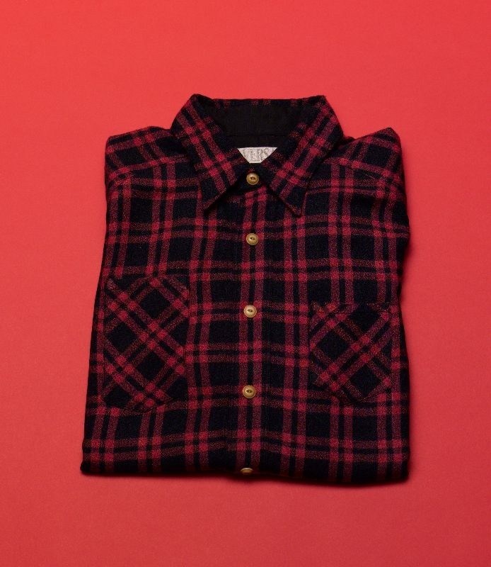 Red and black plaid button-up shirt folded on red background by Haversack.
