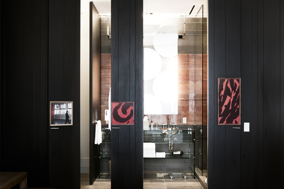 Modern bathroom with black walls, glass shower enclosure, and red abstract artwork above sink.