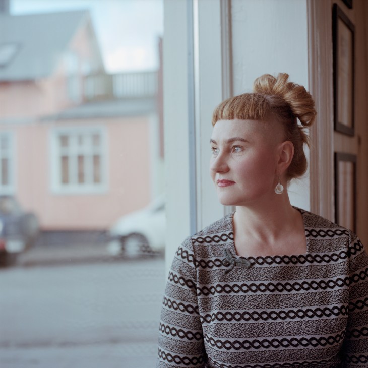 Sonja Grant, owner of Kaffi Midja coffee shop, gazes out a window wearing a patterned Icelandic sweater.