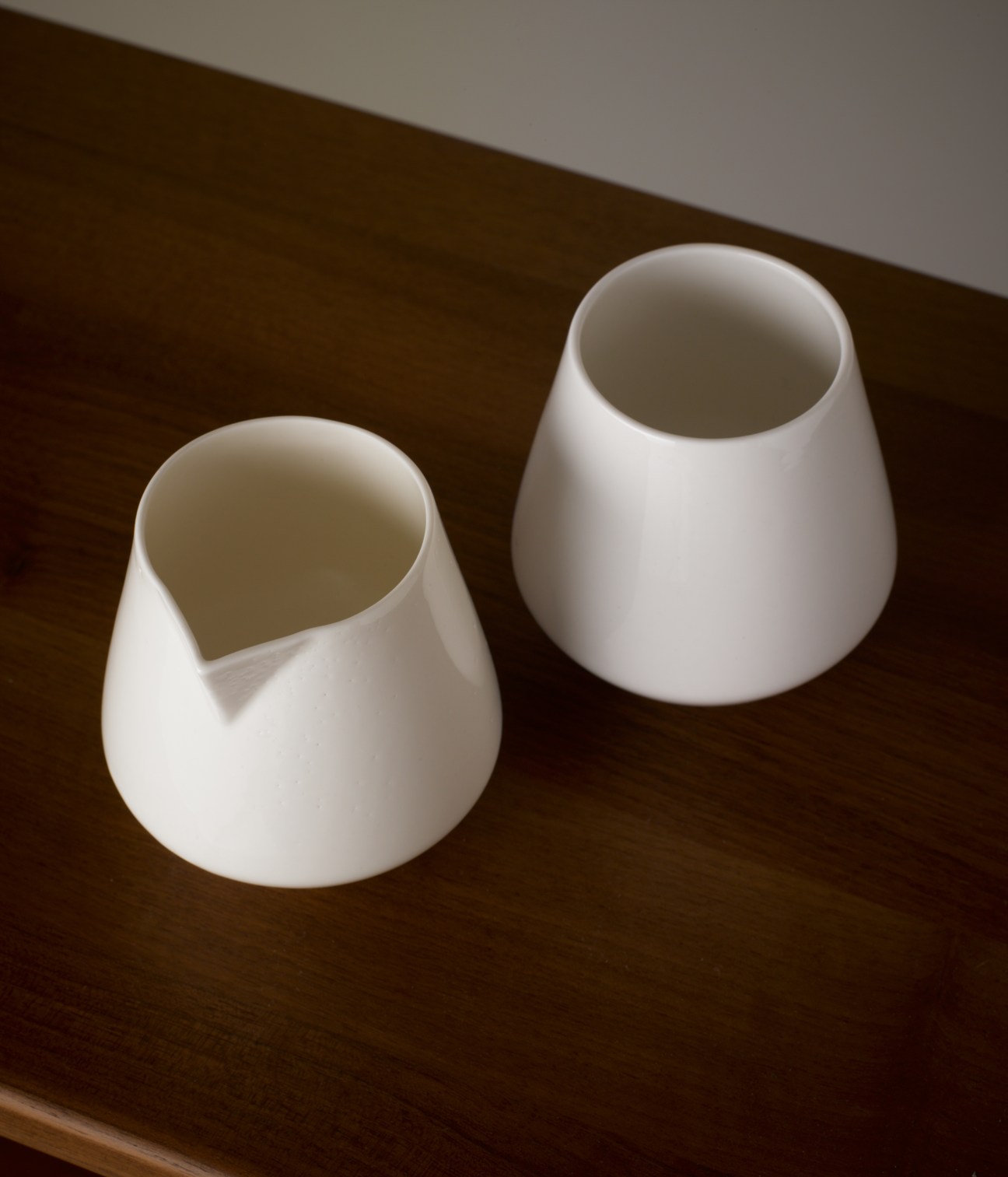 Two white ceramic jugs by Reiko Kaneko on a dark wooden surface.