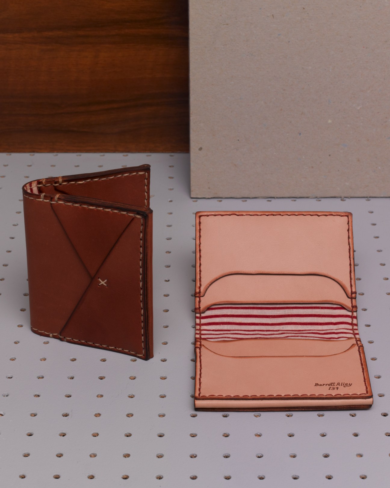 Two handmade leather wallets by Barrett Alley in tan and brown, with saddle stitching and red-and-white cotton lining.