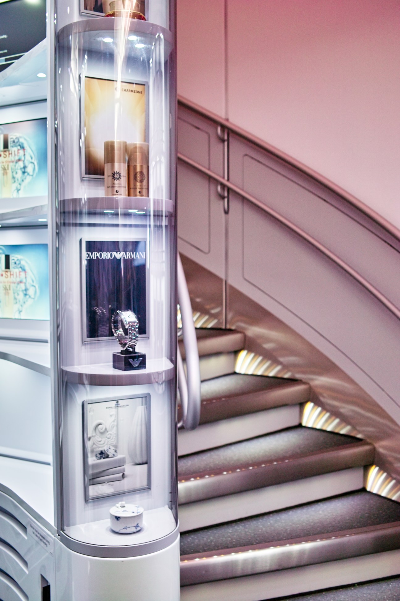 Korean Air's inflight duty-free showcase displaying luxury fragrances and products in a cylindrical display case next to cabin stairs.