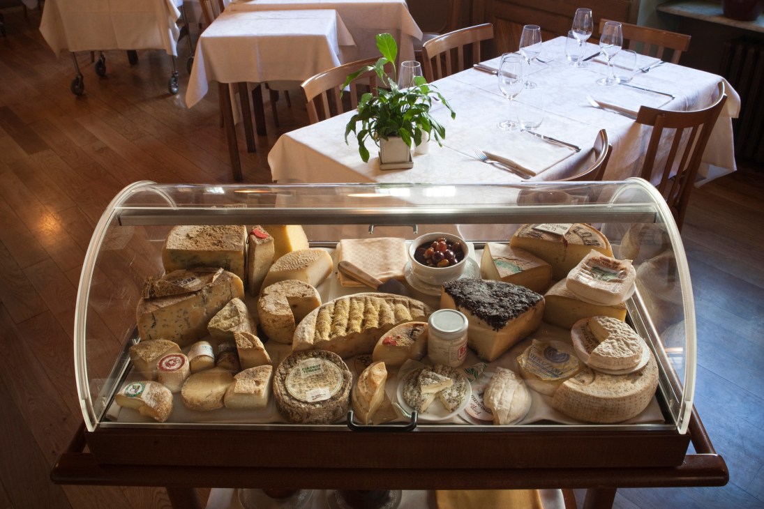 Glass-fronted display case filled with various Italian cheeses at restaurant Tre Galline.