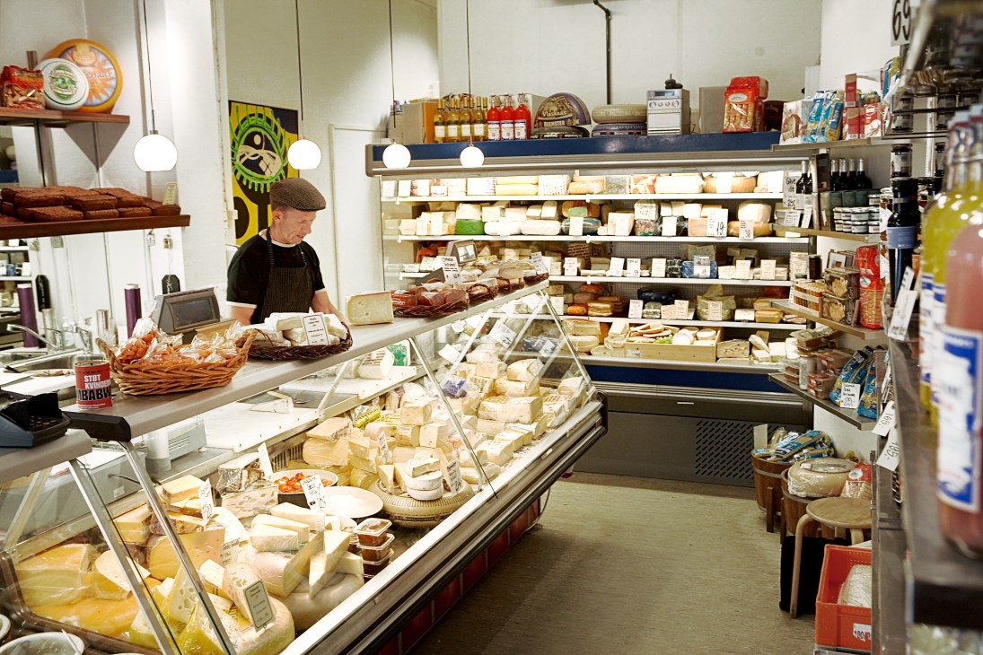 Interior of Helges Ost cheese counter with display cases filled with various cheeses and a shopkeeper behind the counter.