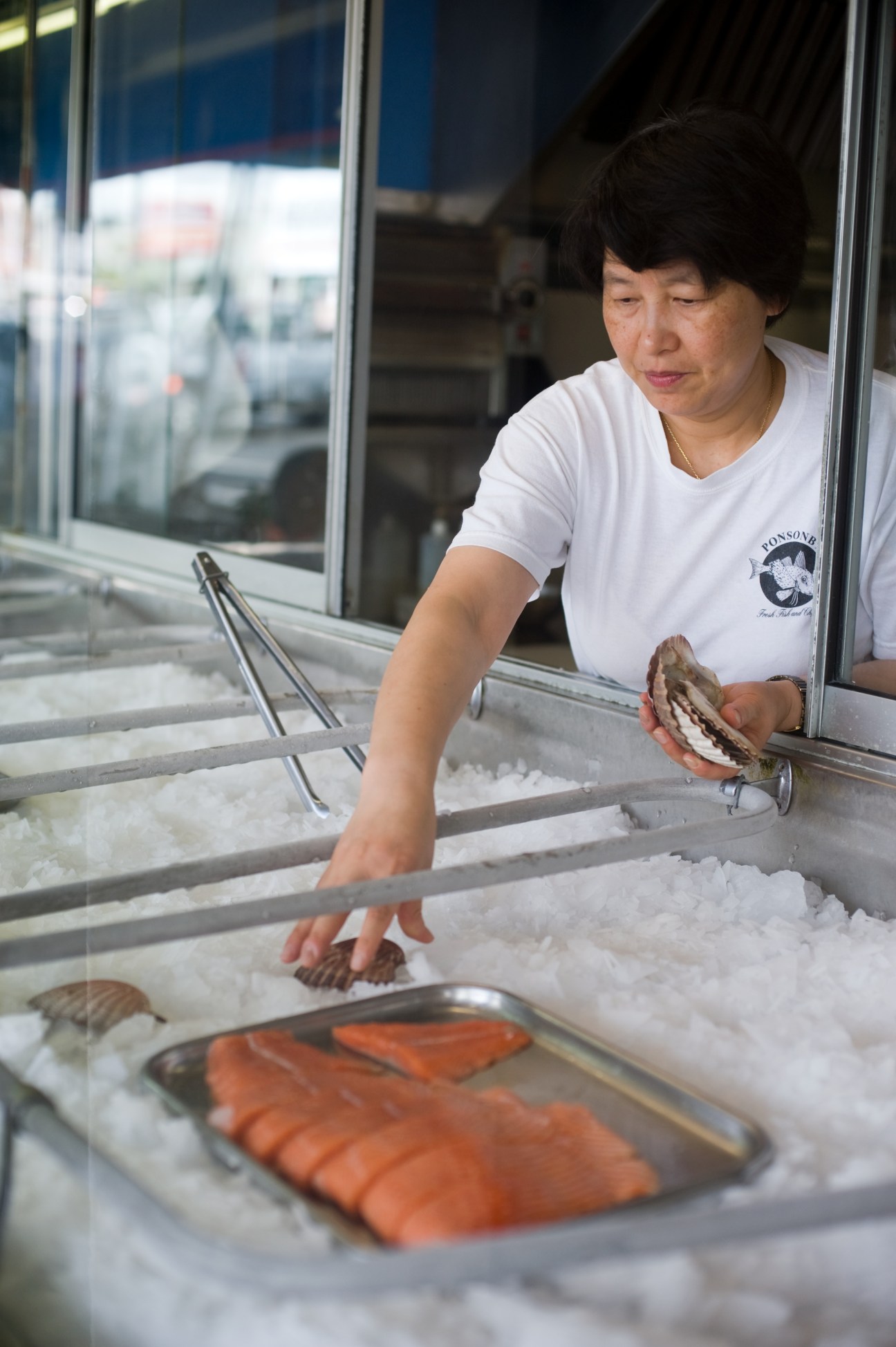 A fishmonger at Ponsonby Fish & Chips selects fresh fish from ice display cases.