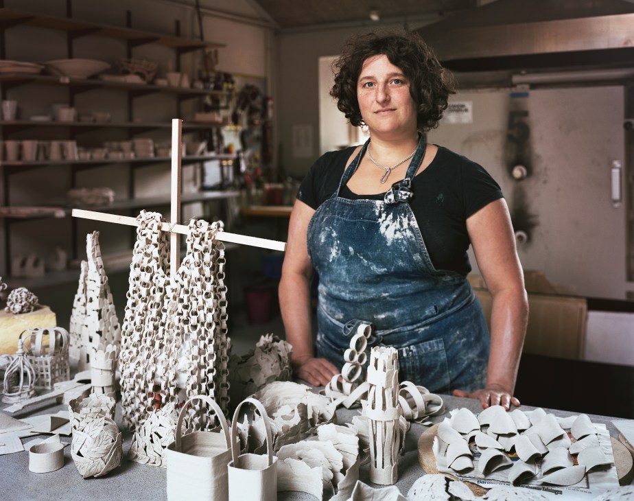 Ceramic student Eva Rosenfeld stands in a studio surrounded by white ceramic sculptural pieces and works-in-progress.