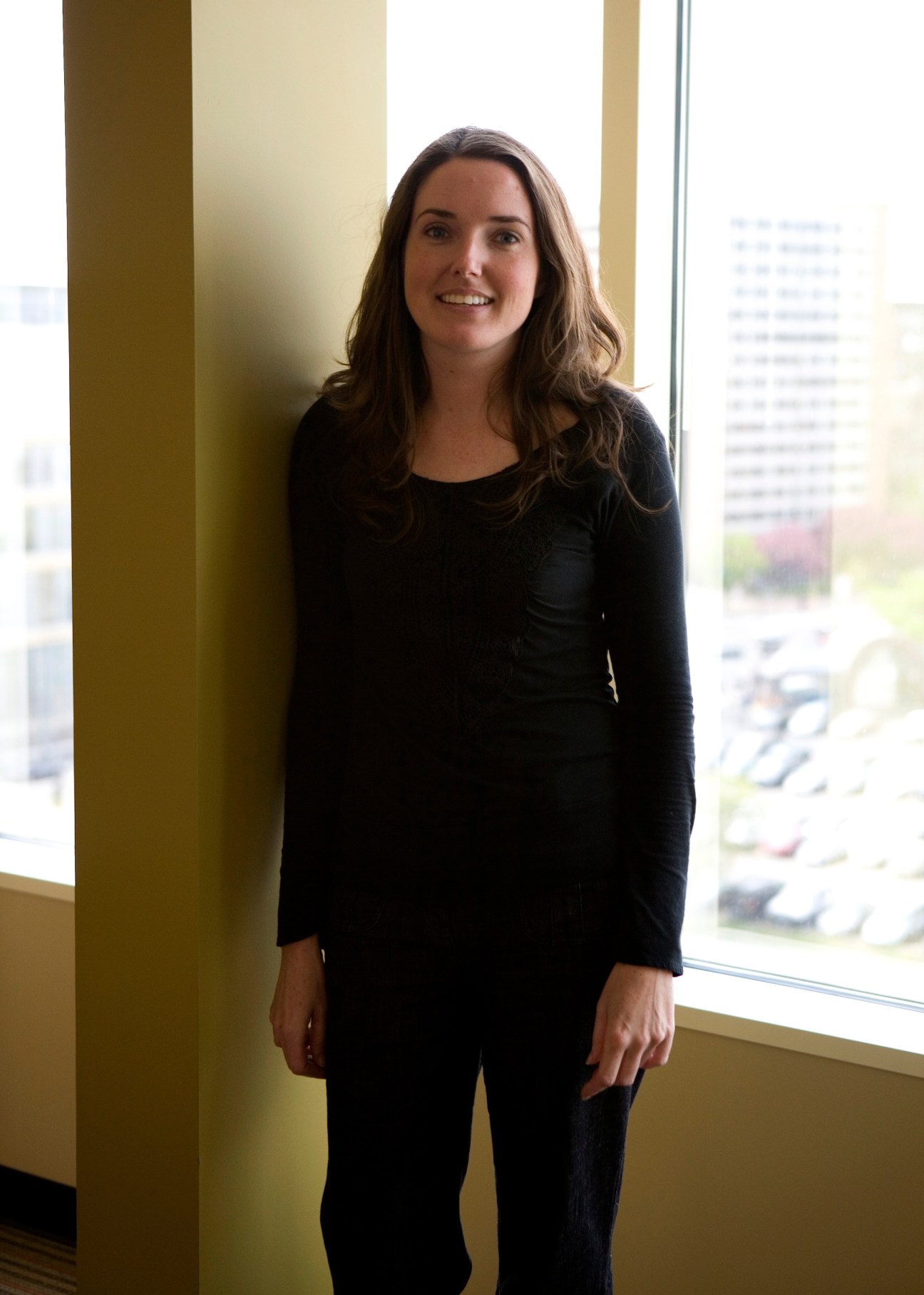 Gretchen Camp, architect at BKV Group, standing by a window in an office with a yellow-green column behind her.