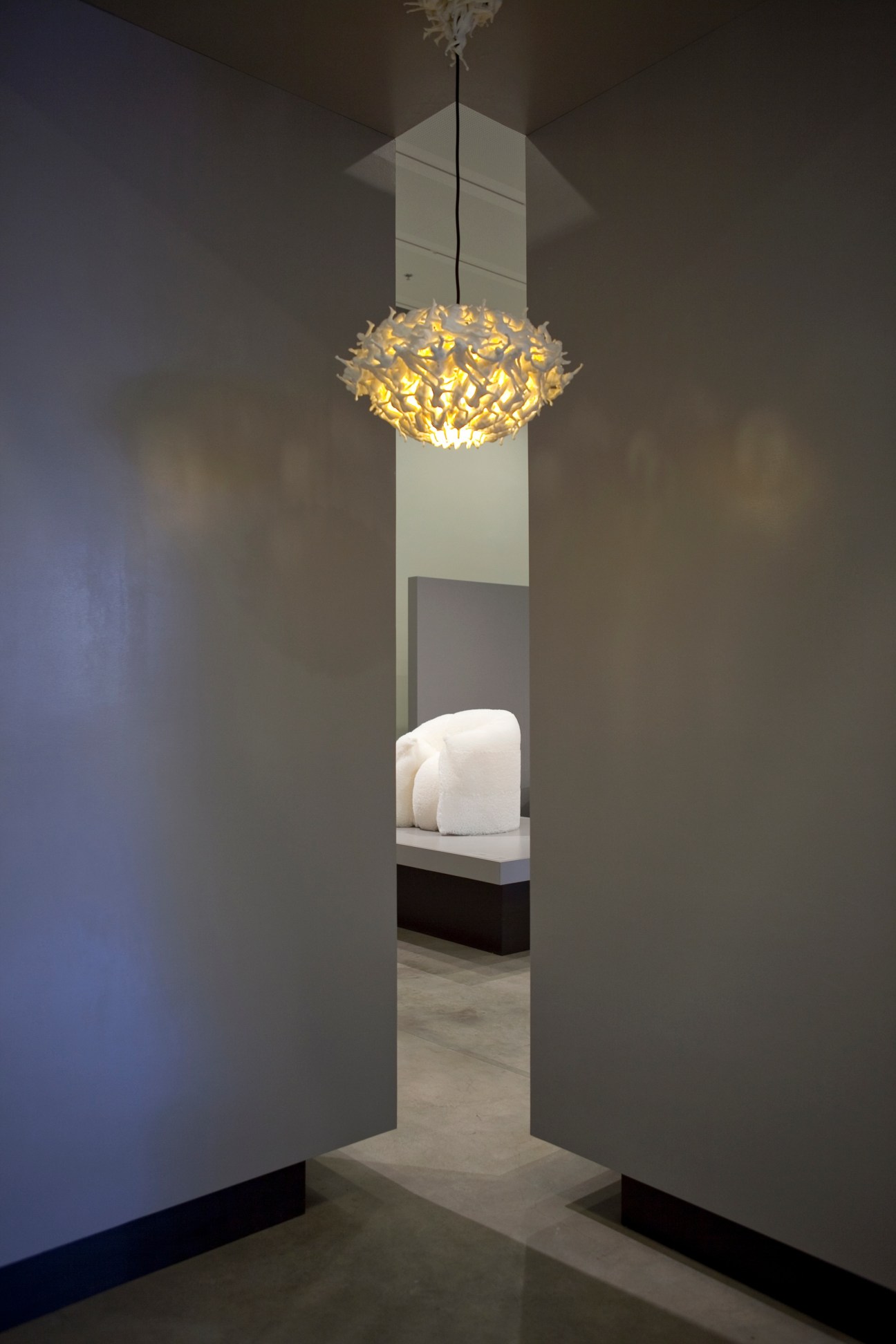 Modern art installation featuring a golden pendant light and white sculptural form in a minimalist gallery space.