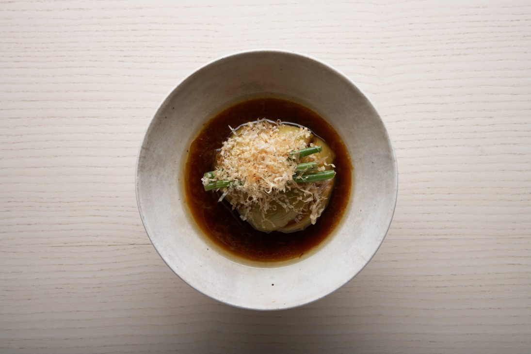Braised aubergine with duck sauce served in a white bowl on a wooden surface.