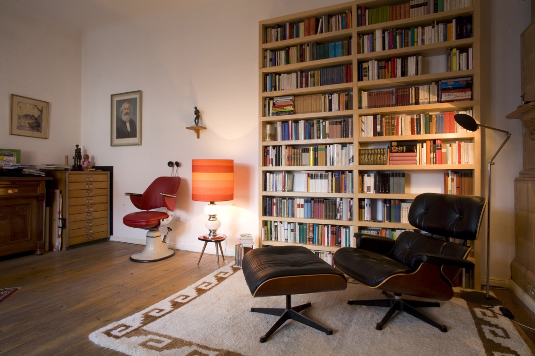 Mid-century modern living room with floor-to-ceiling bookshelf, red chair, black lounge chair and ottoman, and vintage furnishings.