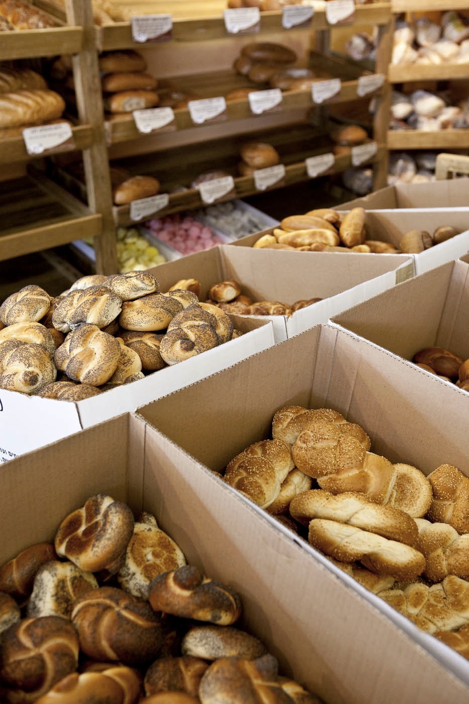 Assorted fresh breads and pastries displayed in white cardboard boxes at a bakery.