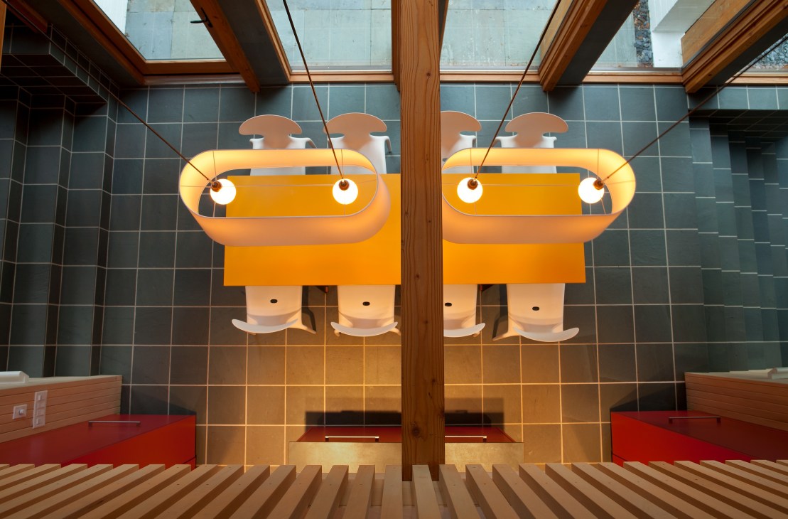 Modern sauna interior with orange pendant lights, wooden beams, and skylight windows overlooking forest.
