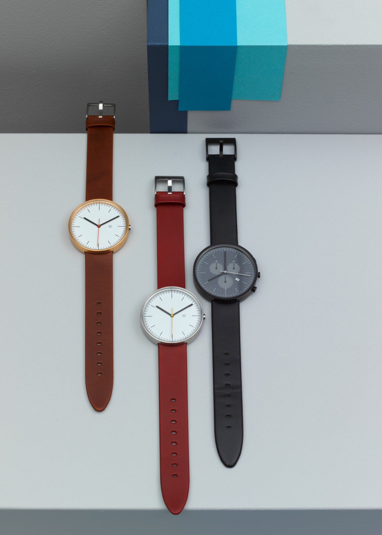 Three Uniform Wares watches with minimalist dial designs in rose gold, silver, and black cases with brown, red, and black leather straps.