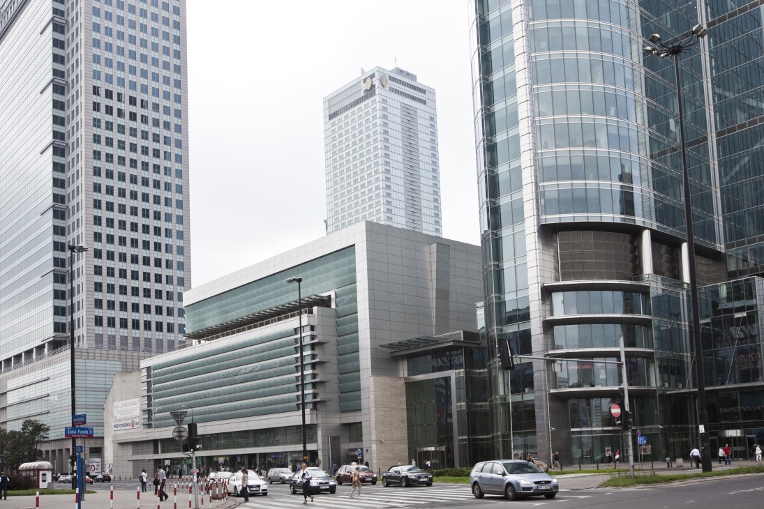 Modern downtown Warsaw street with contemporary office buildings, pedestrians, and vehicles.