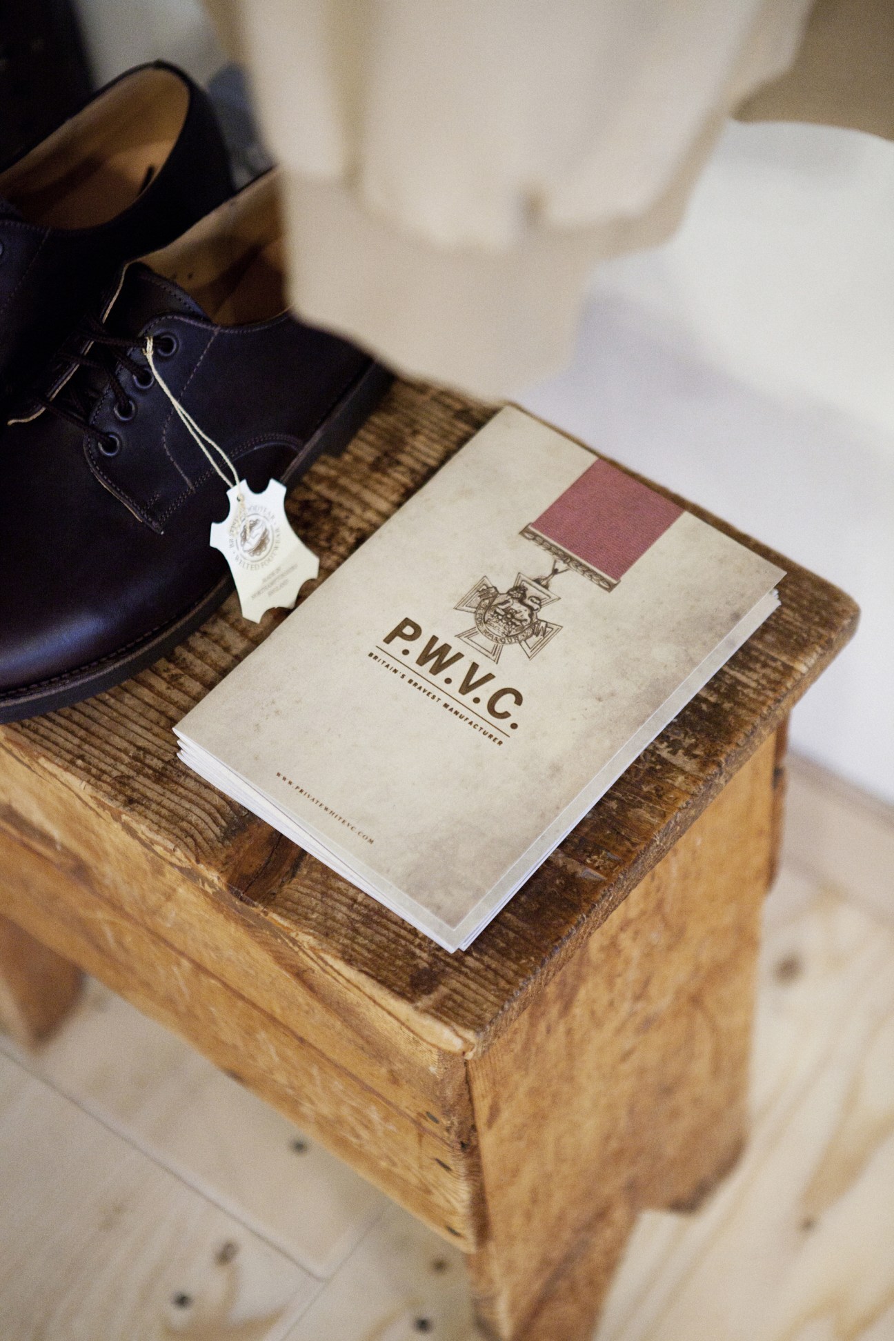 Navy blue leather shoe with white tag next to P.W.V.C. branded packaging on wooden block.