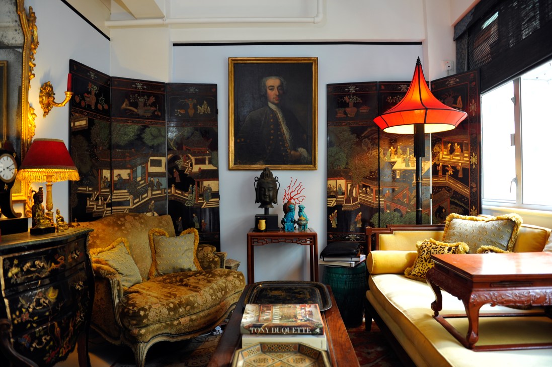 Eclectic living room with ornate gold furniture, Asian art panels, portrait painting, and a bright red pendant lamp.
