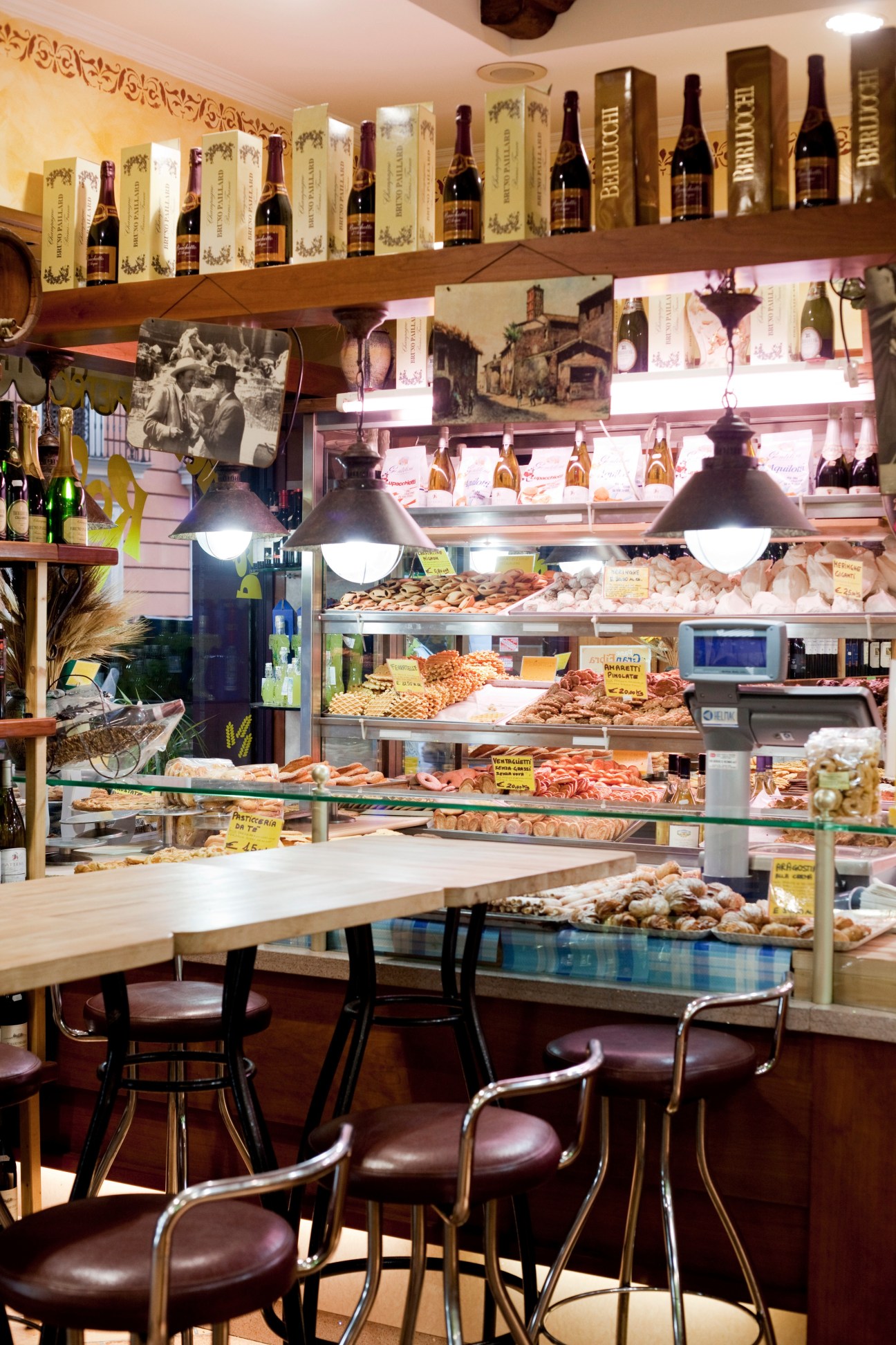 Interior of Roscioli bakery with display cases of baked goods, wine bottles on shelves, and seating area.