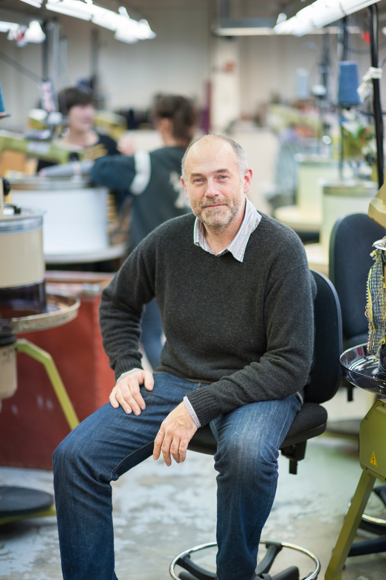 Stuart Maxwell, owner of Esk knitwear, sits in a Scottish factory with production equipment in the background.