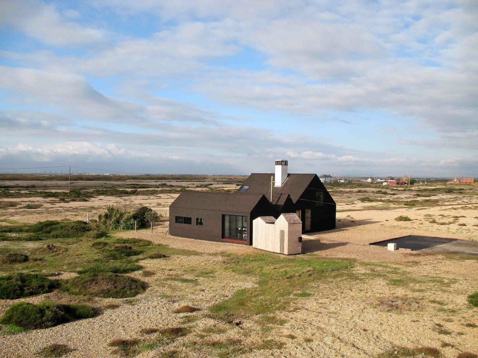 NORD architects' Shingle House with black tarred shingles standing in Dungeness desert landscape with nuclear power station visible in distance.