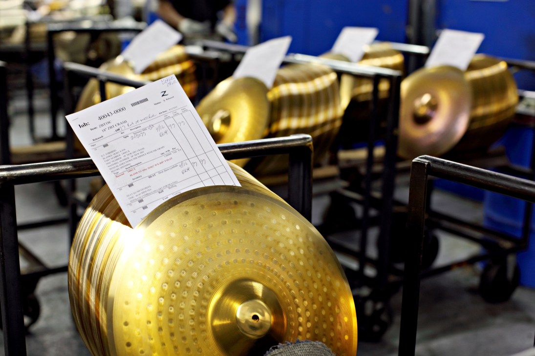 Golden cymbals with quality control test sheets lined up on a rack at Zildjian factory.