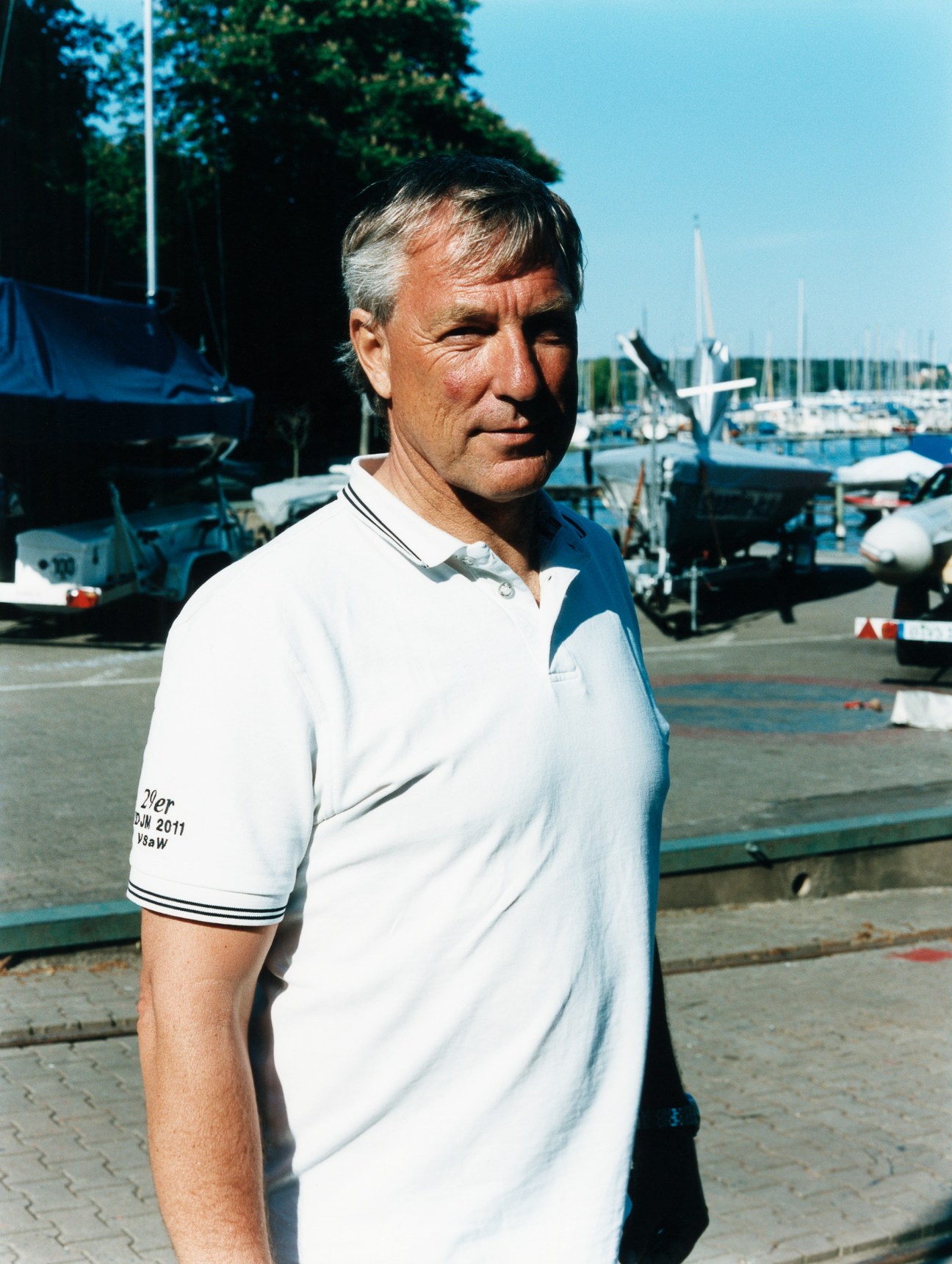 Frank Butzmann, managing director of Verein Seglerhaus am Wannsee sailing club, stands at a marina with moored sailboats behind him.