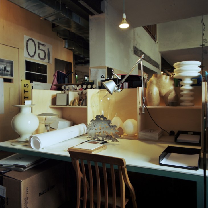 Michele De Lucchi's Tolomeo desk lamp displayed in a studio workspace with ceramic vessels and architectural drawings.