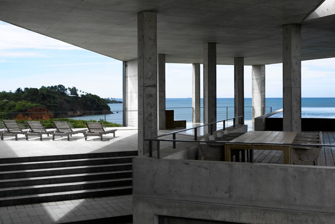 Concrete terrace with loungers overlooking the ocean and tropical coastline designed by Tadao Ando.