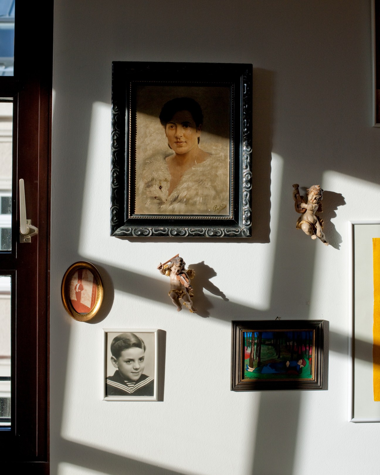 White wall displaying framed artworks and decorative objects including portrait paintings, small sculptures, and photographs.