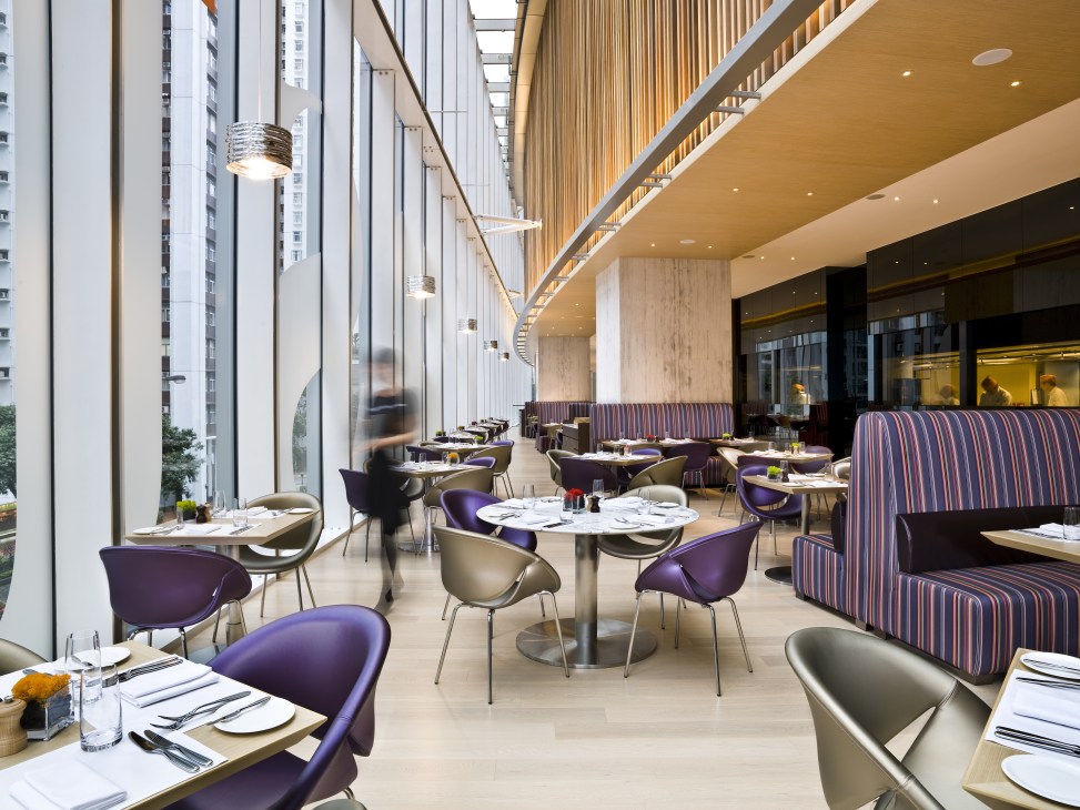 Modern hotel restaurant with floor-to-ceiling windows, purple chairs, and striped banquettes overlooking Hong Kong skyline.