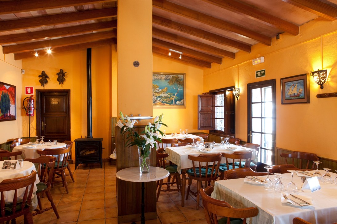 Bright yellow dining room with wooden beams, round tables, white linens, and fireplace at El Bungalow restaurant.