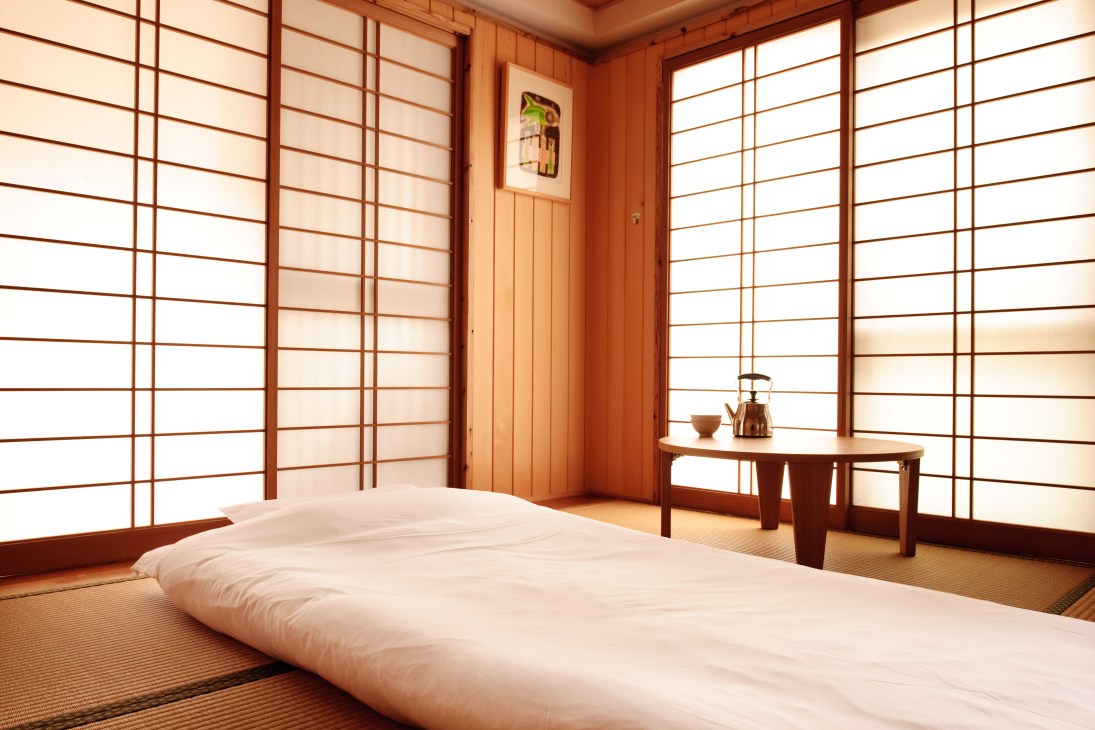 Japanese tatami room with white bedding, wooden furniture, shoji screens, and traditional tea service set.