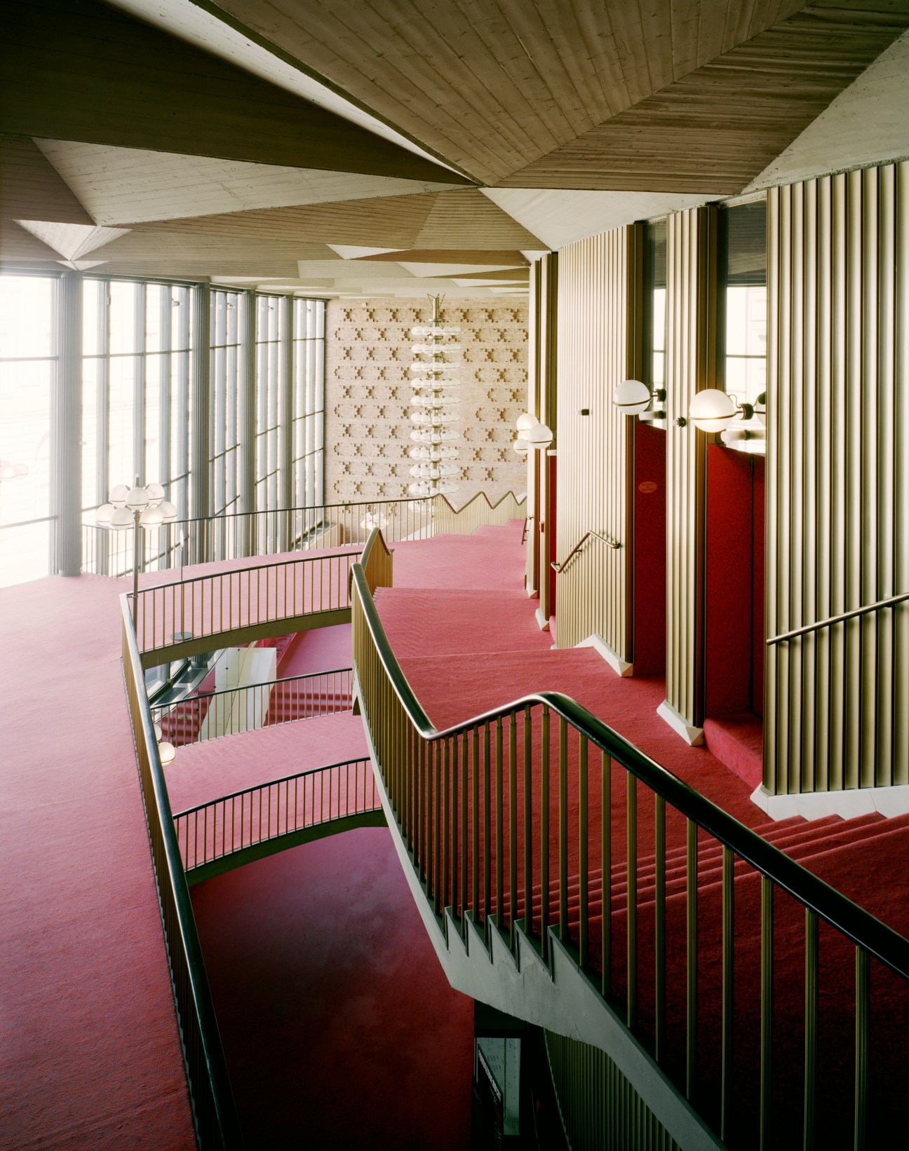 Modernist staircase with pink and red carpeting, metal railings, and geometric ceiling design at Teatro Regio.