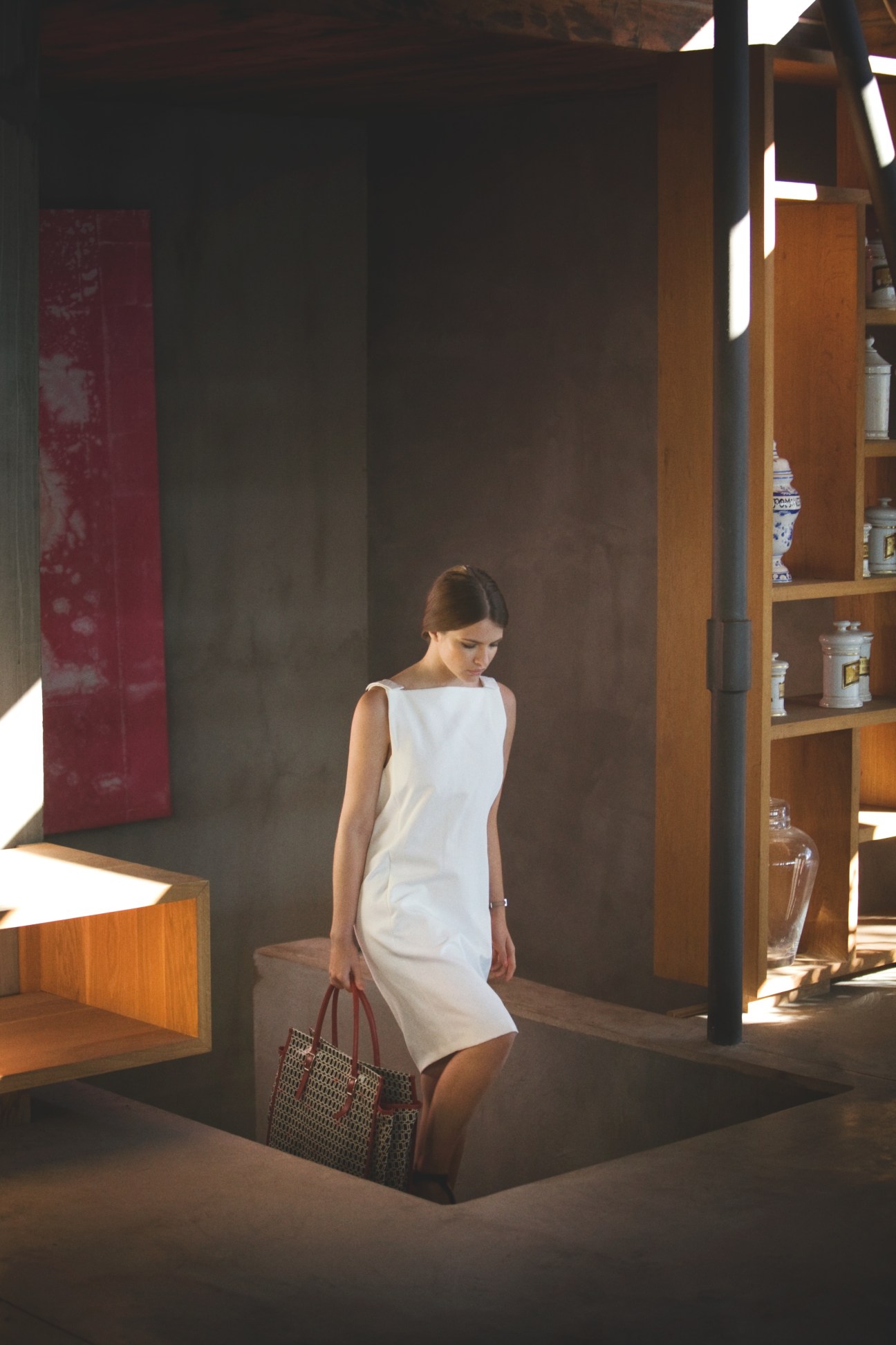 Woman wearing a white sleeveless Bottega Veneta dress and carrying a Roger Vivier bag in a modern interior space.