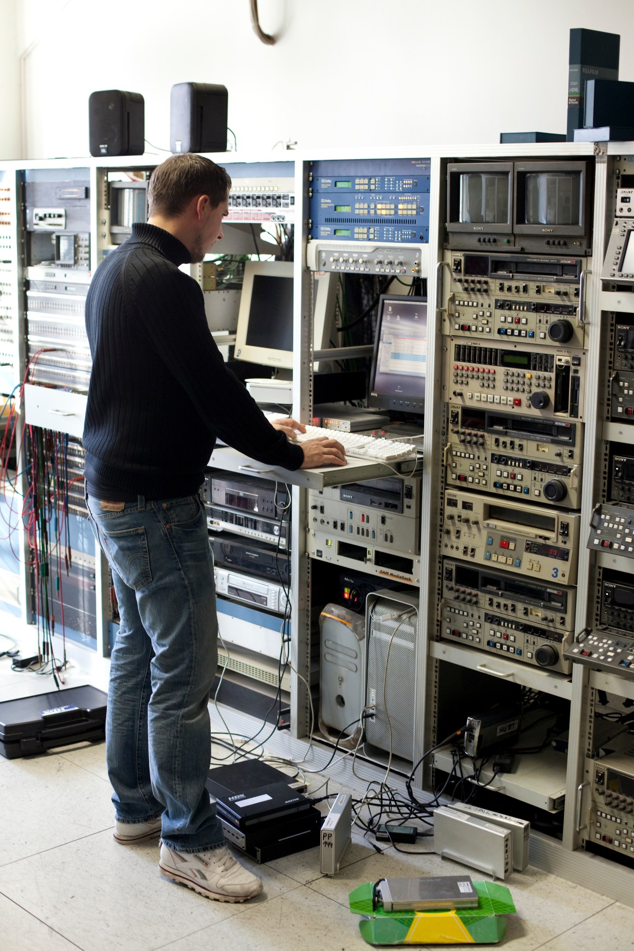 A technician stands at a control panel with professional audio equipment and monitors in a Berlin dubbing studio.