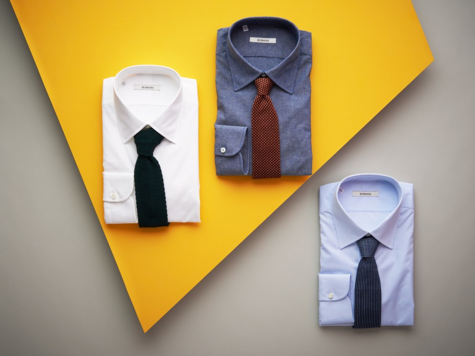 Husbands menswear collection displaying folded dress shirts in white and blue with coordinating ties on yellow and gray background.