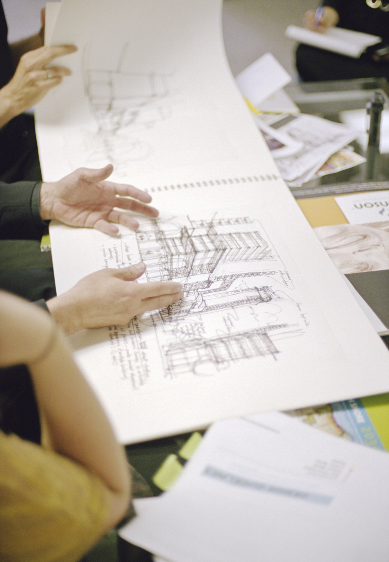 Two people review architectural sketches and drawings spread across a table during a planning discussion.