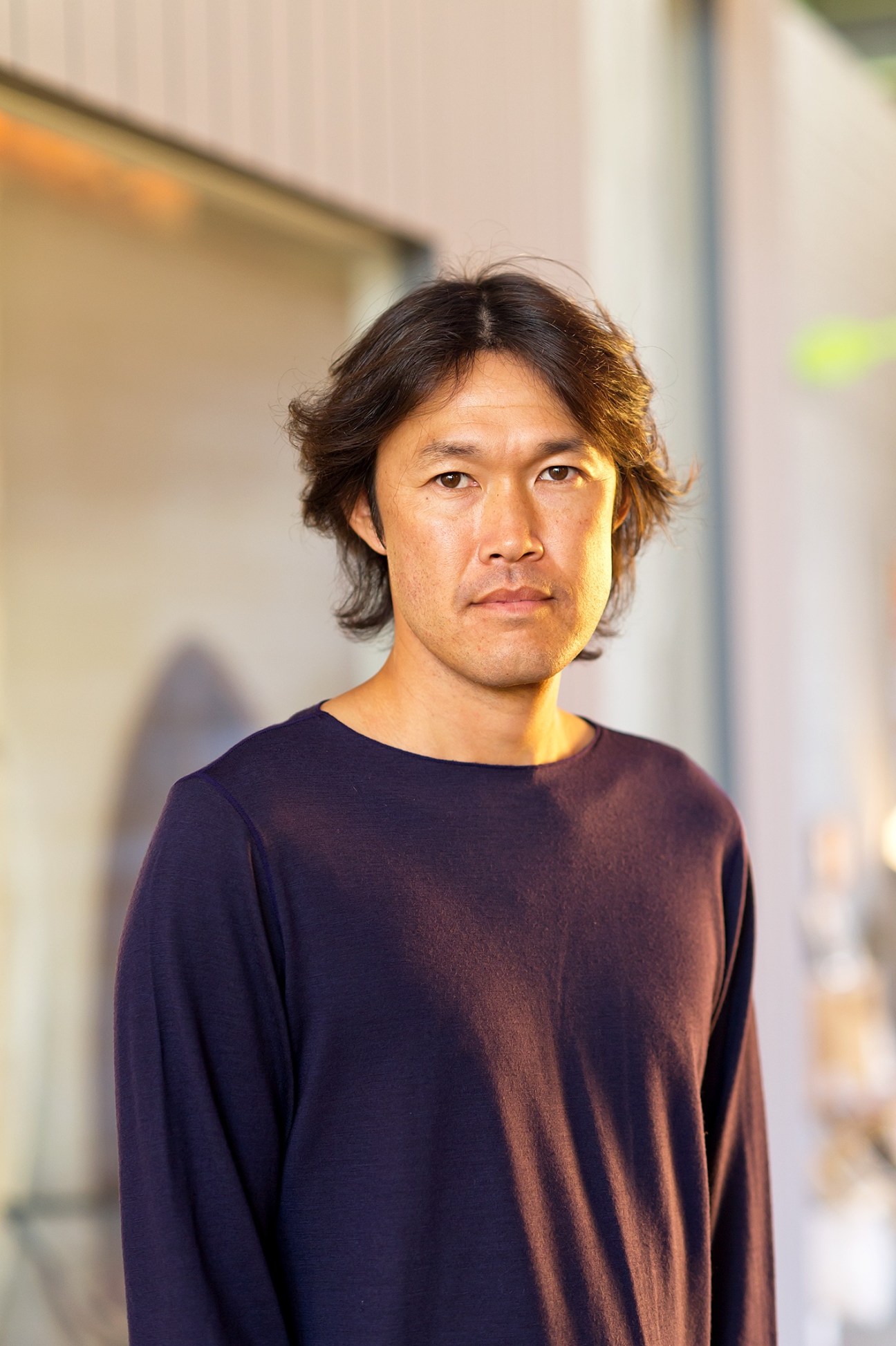 Portrait of Kazutoyo Yamamoto, founder of Newland, wearing a dark long-sleeved shirt against a blurred urban background.