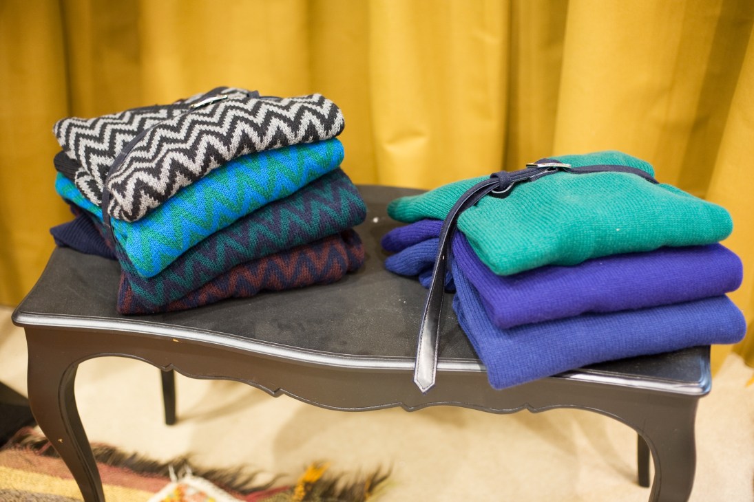 Colorful knit scarves and accessories displayed on a black bench against a yellow backdrop.
