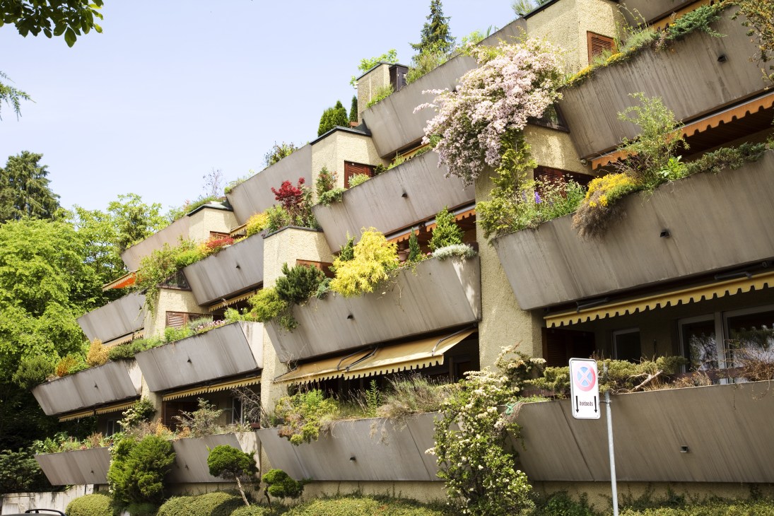 Tiered residential building with cascading balconies and abundant flowering plants and greenery.