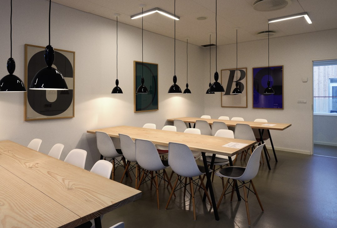 Modern canteen with wooden tables, white chairs, black pendant lights, and framed artwork on walls.