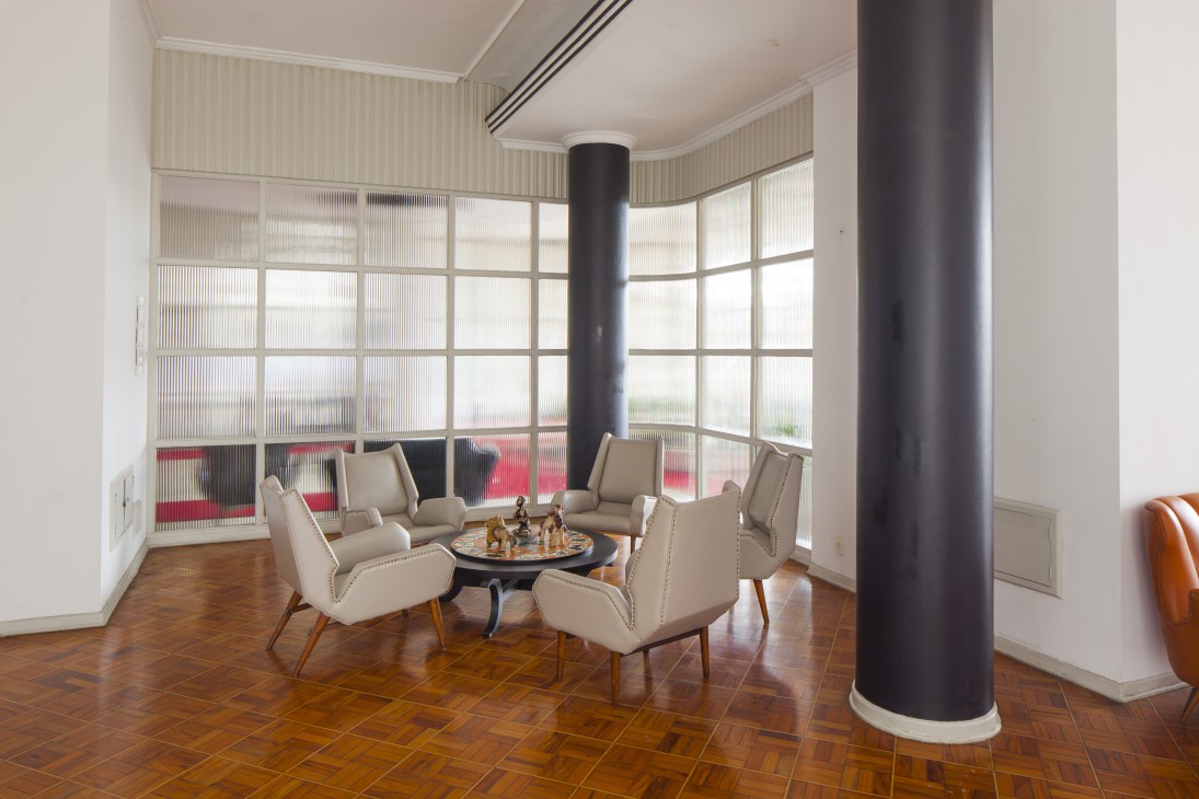 Mid-century modern games room with cream armchairs, black table, and large grid windows overlooking the beach.