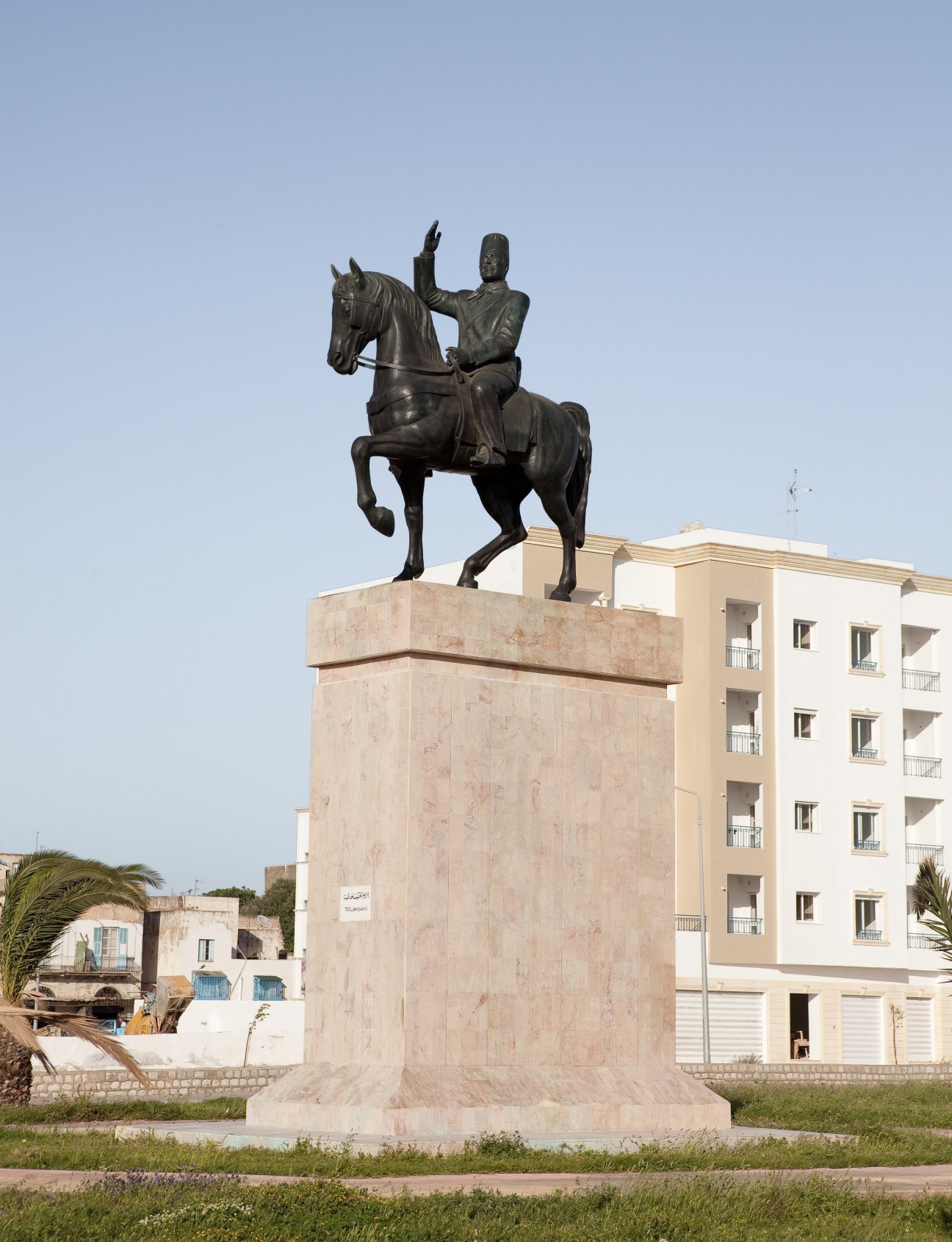 Bronze equestrian statue of Habib Bourguiba on a stone pedestal in a public square, with a cream-colored building behind it.