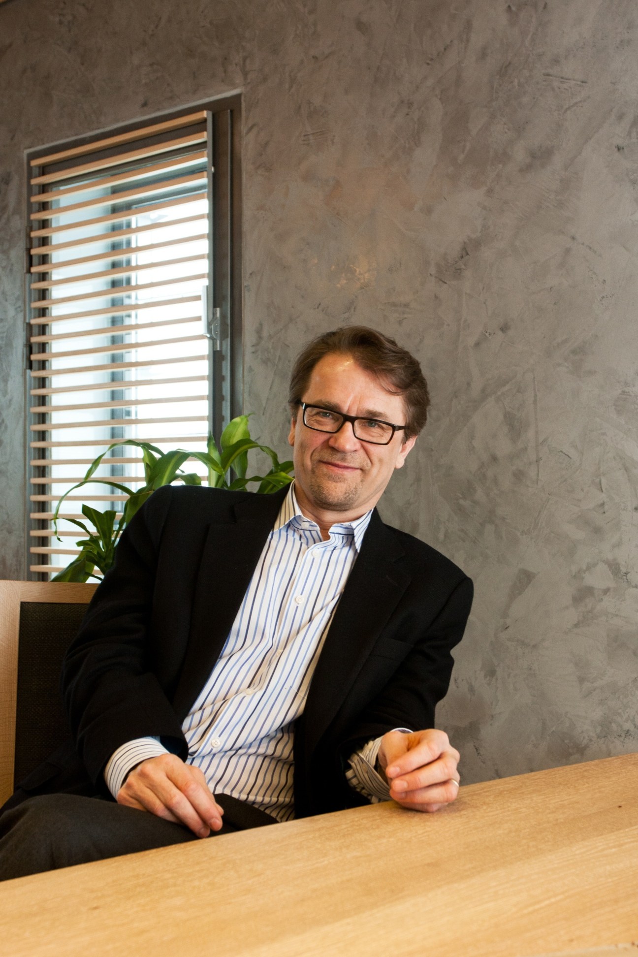 Mikko Kosonen, president of Sitra, sitting at a wooden desk in an office with concrete walls and a slatted window.
