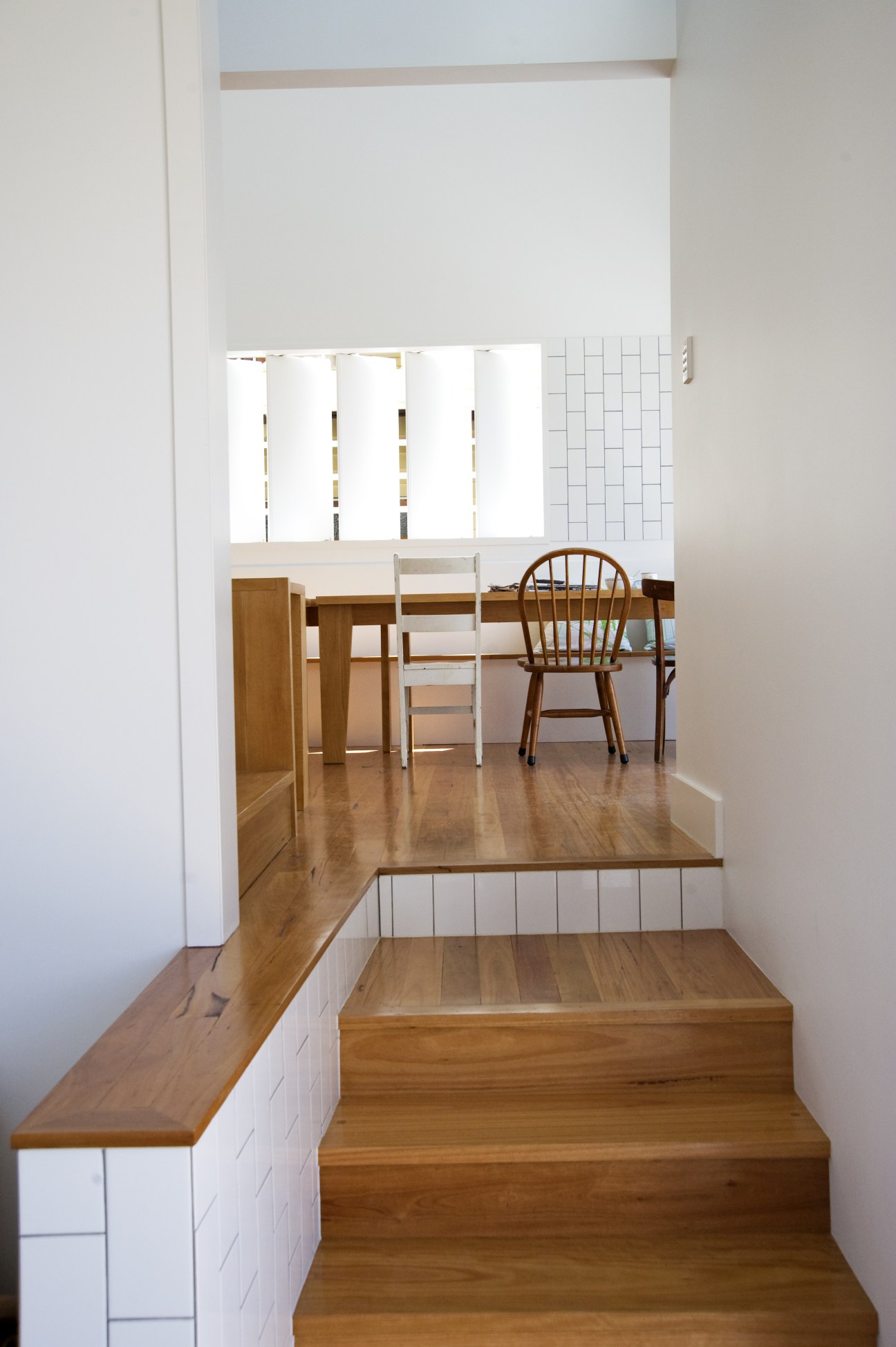 Wooden staircase with hoop pine floors leading to a bright dining room with wooden table and chairs.